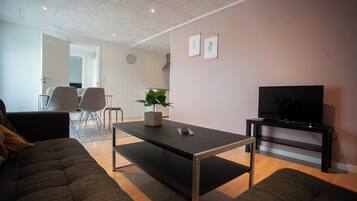 A modern living room with a sofa, a coffee table, a TV stand, and a potted plant.