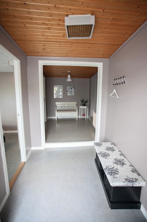 A hallway leading to a room with a wooden ceiling, a bench, a small table, and a wall-mounted coat rack.