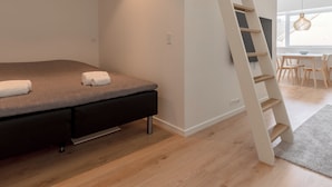 A modern bedroom with a bed, a wooden floor, a white wall, and a skylight.