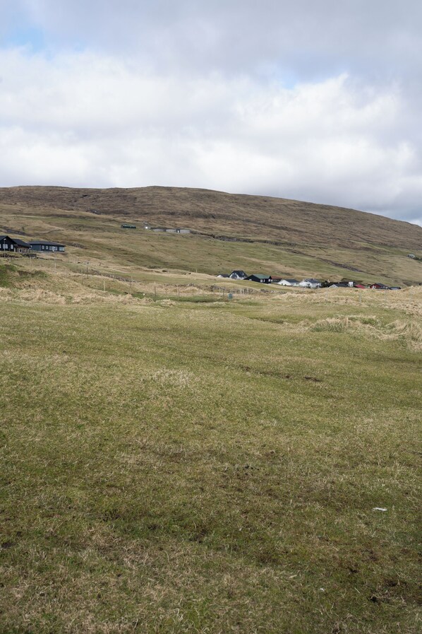 A rural landscape with a grassy field and a few houses on a hill. - Brand New / Airport / Rentyourcar / Free Parking (Miðvágur)