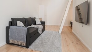 A modern living room with a black sofa, grey rug, and a TV mounted on the wall.