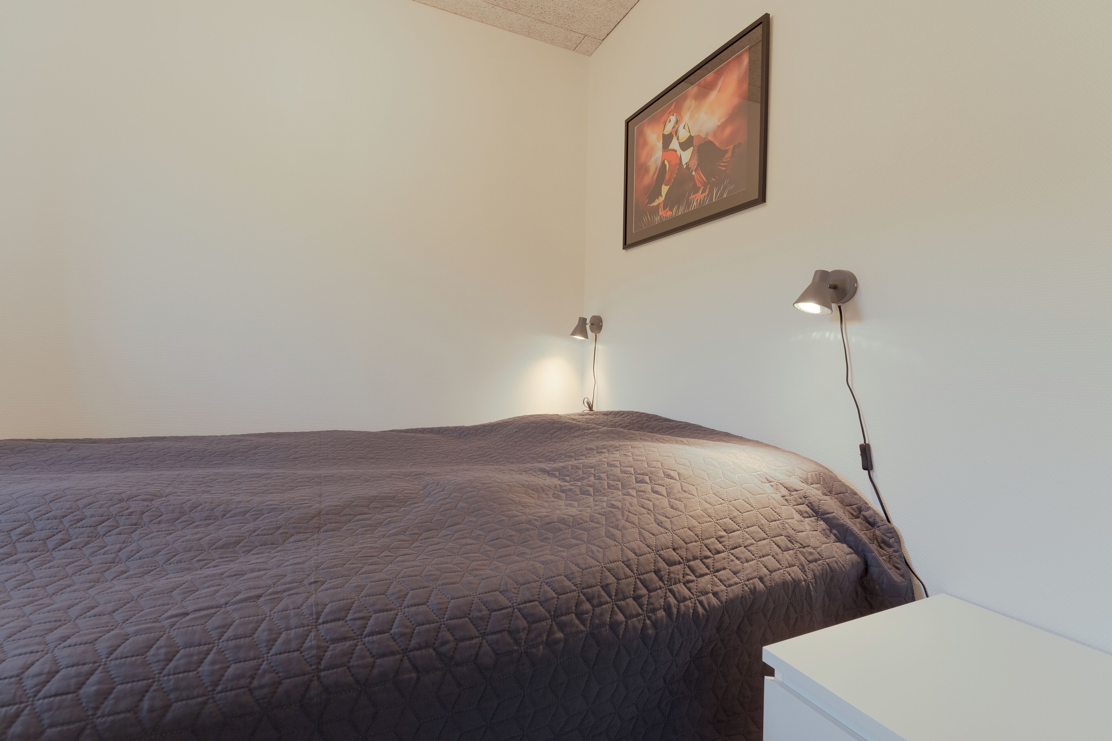 A bedroom with a large bed, two bedside lamps, and a framed picture on the wall.