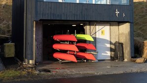 A two-story building with a garage door, a balcony, and several kayaks stored inside. - Unique Boathouse - Central - Kajak - Fitness (Strendur)