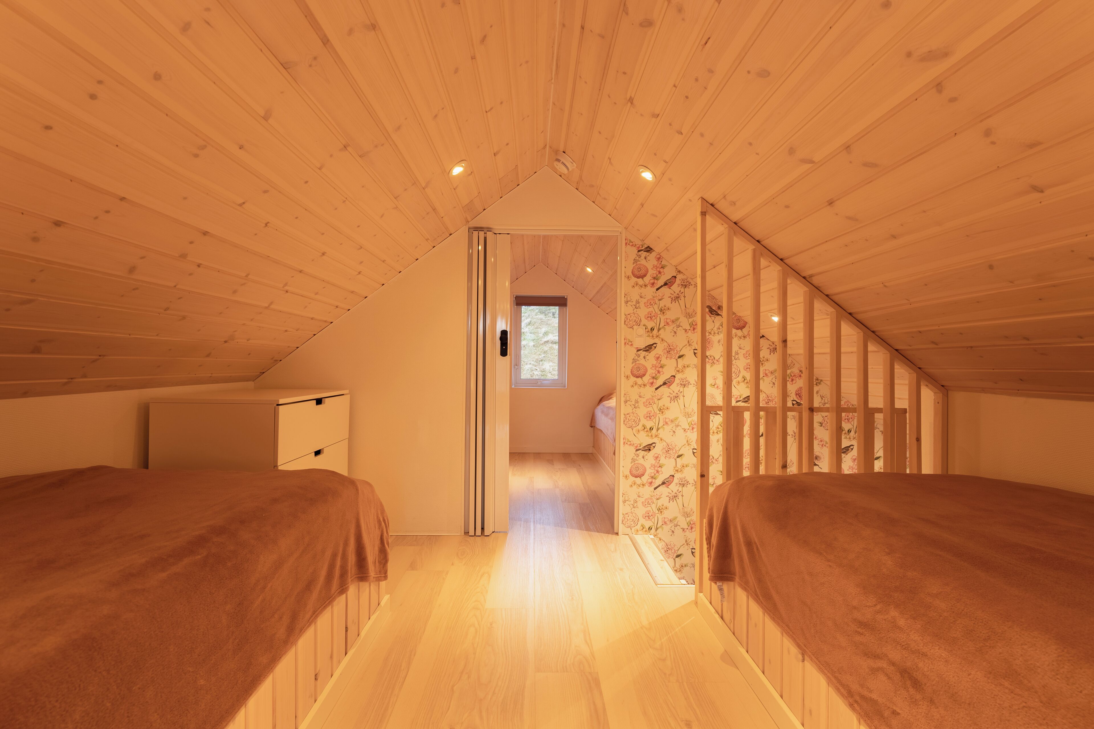 A bedroom with two beds, wooden ceiling, a small window, and a door leading to another room.