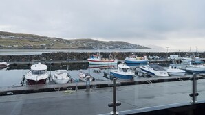 A harbor with several boats docked, a stone wall, and a view of a distant town across the water. - Unique Boathouse - Central - Kajak - Fitness (Strendur)