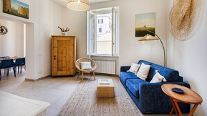 Ein Wohnzimmer mit blauem Sofa, Korbsessel und Holzschrank.