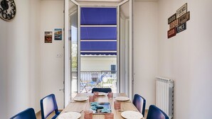 Ein Essbereich mit einem Holztisch, gedeckt für vier Personen, blauen Stühlen und Blick auf einen Balkon mit blauem Markisenstoff.