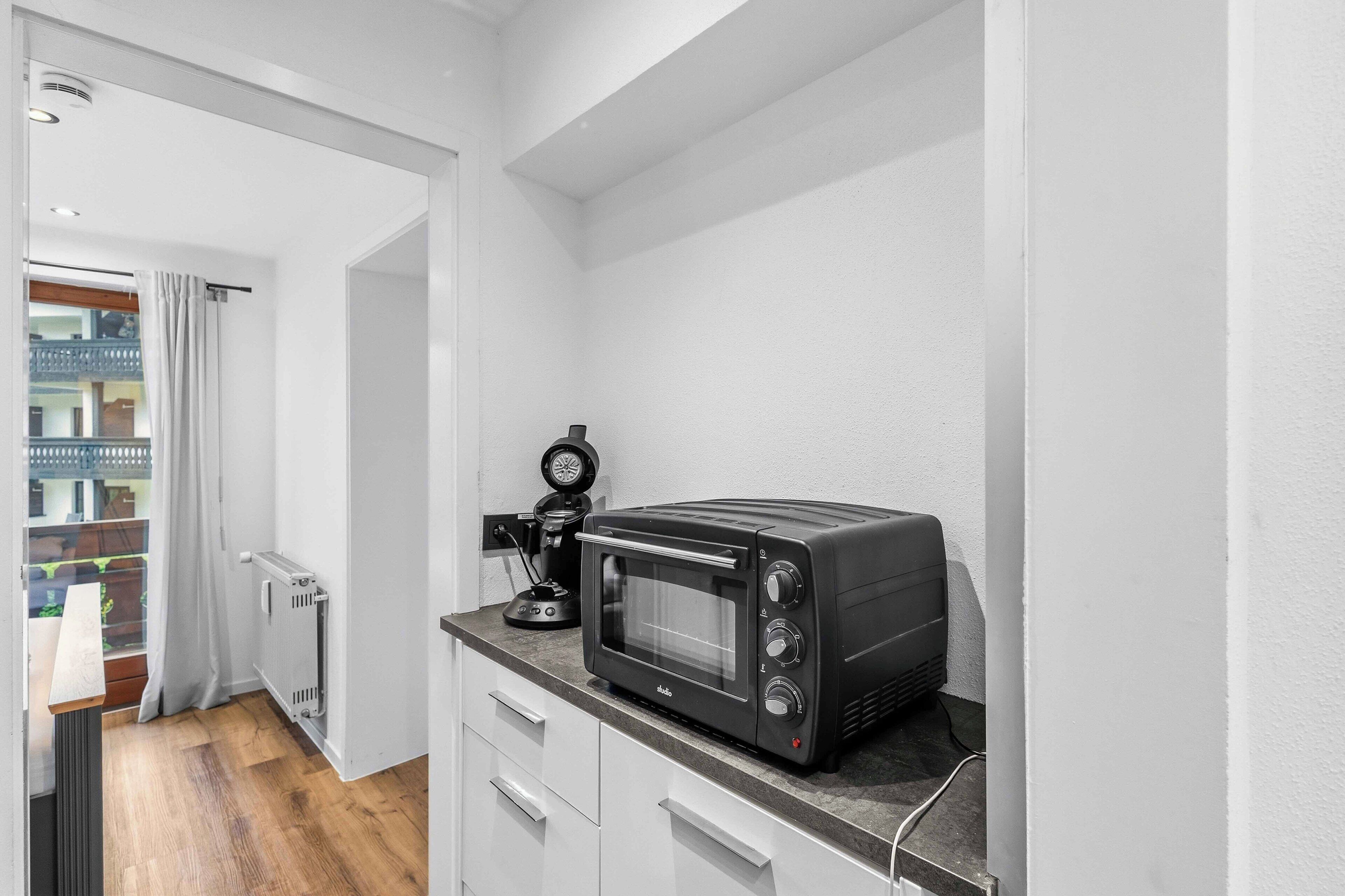Eine Küchenzeile mit einem schwarzen Toaster auf der Arbeitsplatte, einer Kaffeemaschine und Blick auf einen Balkon mit Geländer.