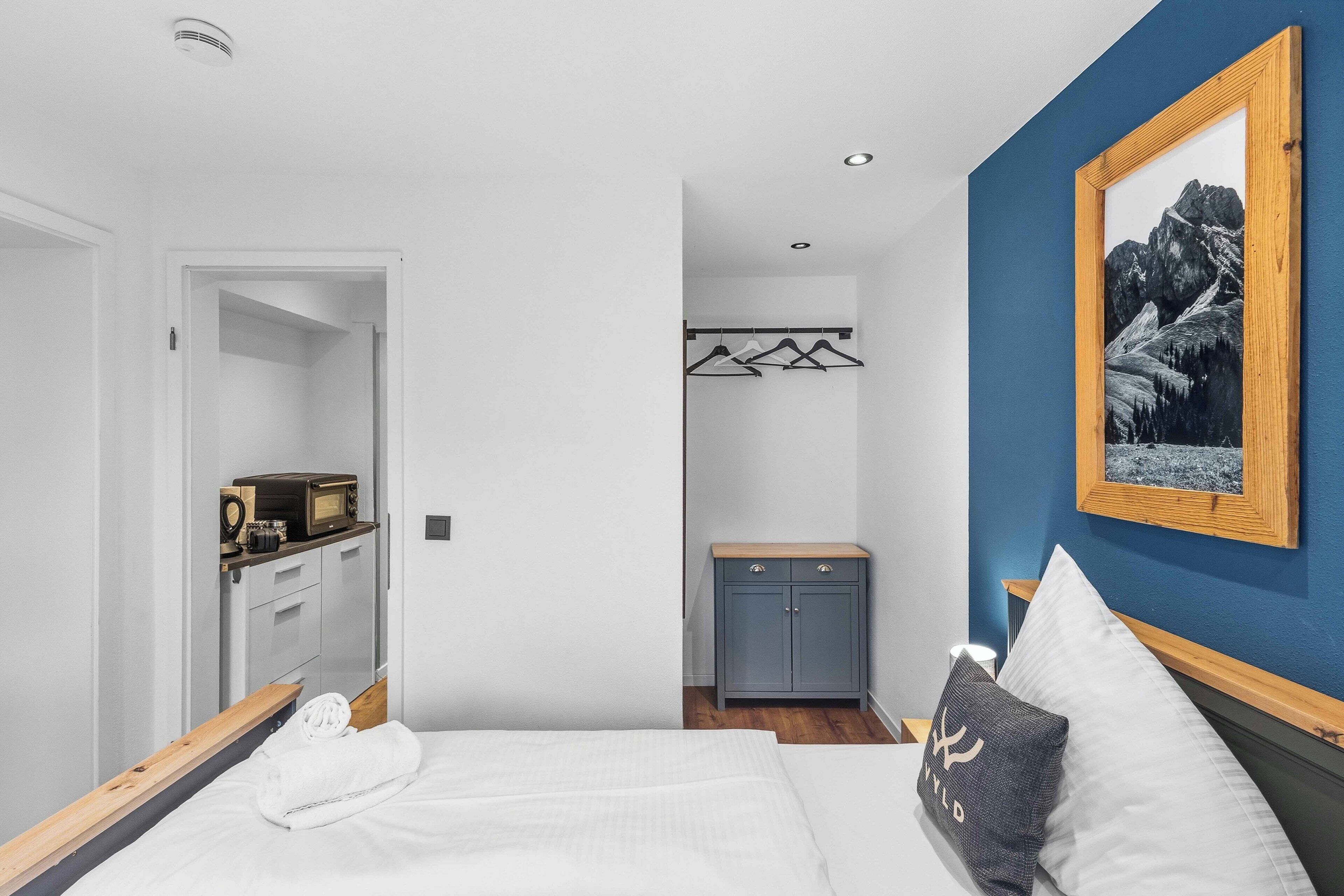 A bedroom with a bed, a wardrobe, a coat rack, and a framed picture on the wall.