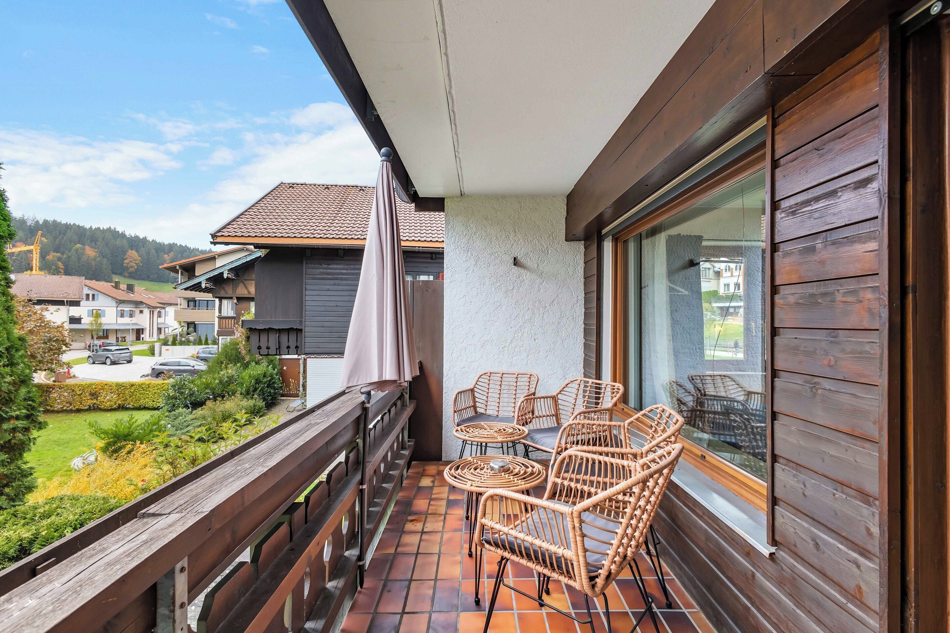 Ein Balkon mit Korbmöbeln, Blick auf eine Wohngegend und Holzgeländer.