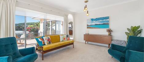 A modern living room with a sofa, two armchairs, a wooden cabinet, and a painting on the wall.