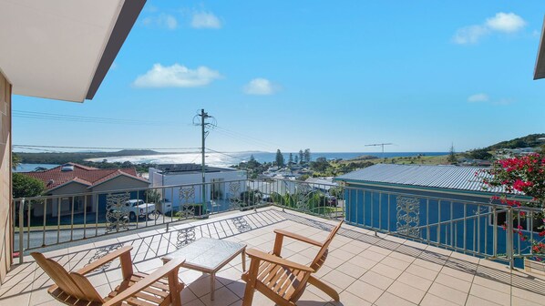 A balcony with a view of the ocean, a tiled patio, and a blue building.