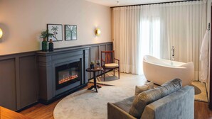 Un salon avec une cheminée, un canapé, un tapis rond, un fauteuil et une baignoire.