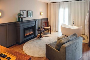 Una sala de estar con chimenea, un sofá, un tapete redondo, un sillón y una bañera.