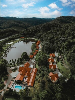 An aerial view of a resort with a swimming pool, connected buildings, and a lake.