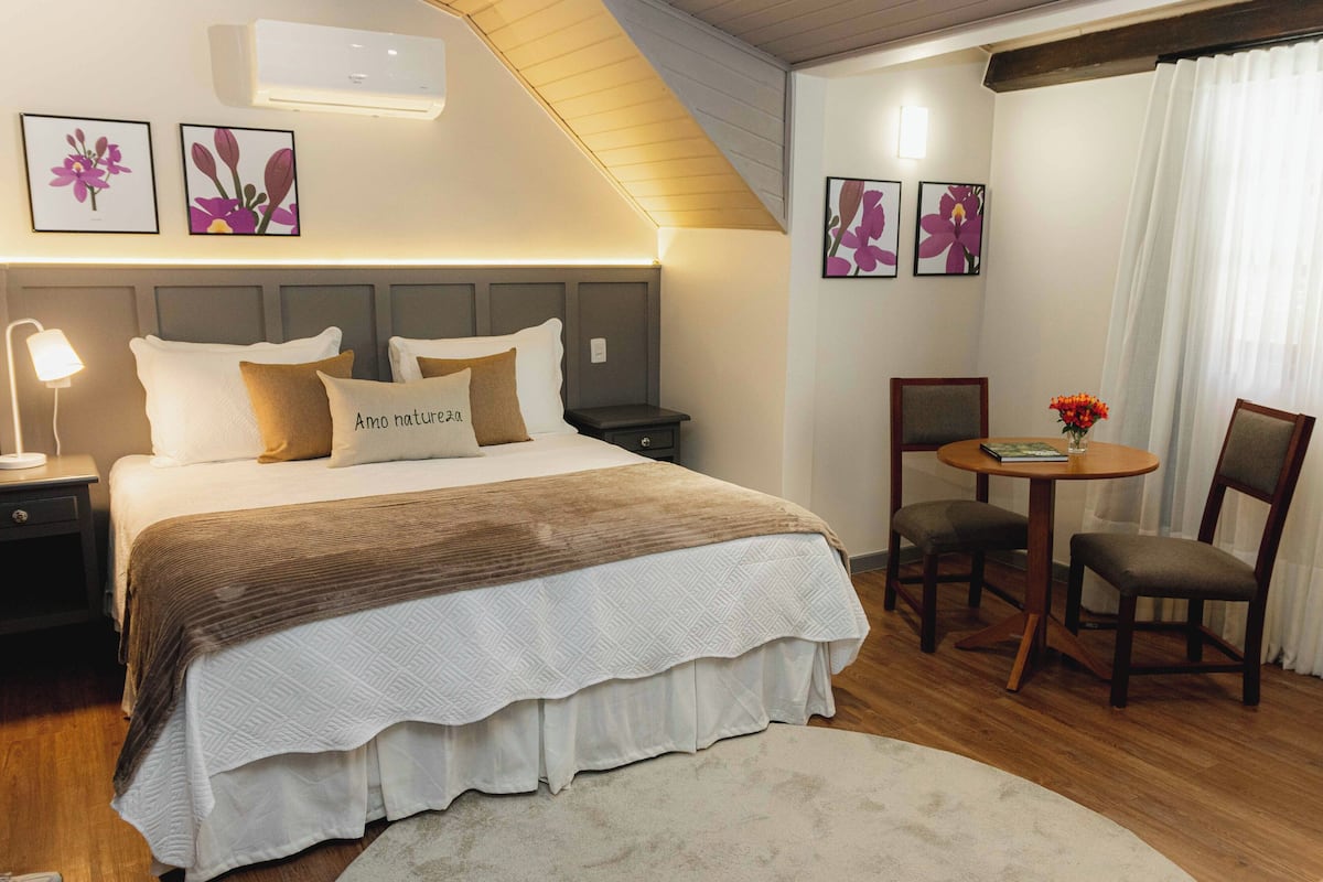 A bedroom with a bed, bedside tables, a round table with chairs, and wall-mounted air conditioning.