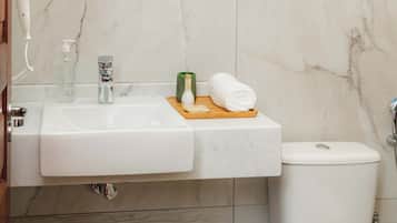 A bathroom with a white sink, mirror, and toilet. There is a towel and a bottle on the sink.