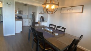 Een eethoek met een houten tafel en stoelen, een kroonluchter en een keuken op de achtergrond.