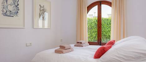 A bedroom with a bed, pillows, a window with curtains, and two framed artworks on the wall.