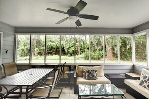A sunroom with a ceiling fan, large windows, a dining table, and seating areas.