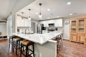 A modern kitchen with a marble island, stainless steel appliances, wooden cabinets, and pendant lighting.