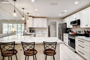 A modern kitchen with white cabinets, a large island with bar stools, stainless steel appliances, and pendant lighting.