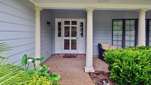 Uma casa com varanda, porta branca e um pequeno jardim.