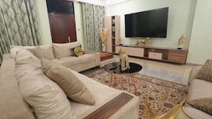 A living room with a beige sofa, a coffee table, and a TV on the wall. - Mercy Royal Heights (Kumasi)