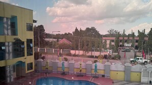 A swimming pool with a red deck, surrounded by a low wall and umbrellas. - Mercy Royal Heights (Kumasi)