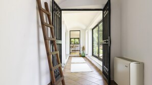 A hallway with a wooden ladder leaning against the wall, a radiator, and a large window with a view of greenery outside.