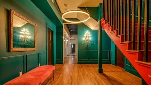 Un pasillo con un banco rojo, paredes verde mar y una escalera roja.