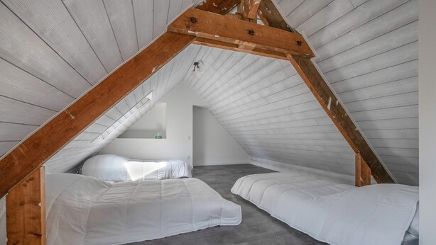 A small attic bedroom with two beds, wooden beams, and a sloped ceiling.