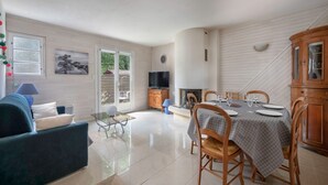 A spacious living area with a sofa, a glass coffee table, a dining table set for four, and a television.