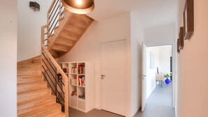 Et moderne interiør med en trætrappe, en hvid dør og en gang, der fører til et spiseområde.