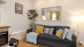 A modern living room with a dark grey sofa, a large mirror, and a potted plant. - Live In The Heart Of Bustling Camden (London)