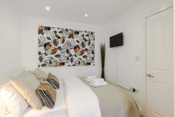 Ein Hotelzimmer mit Bett, Kissen, einem Flachbildfernseher und einem Wandbild.