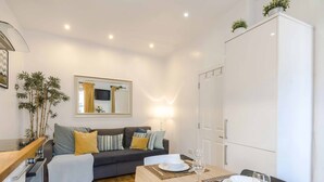 A modern living room with a sofa, a dining table set for two, and a TV mounted on the wall. - Live In The Heart Of Bustling Camden (London)