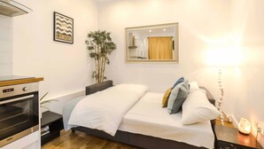 A bedroom with a bed, a bedside table, a lamp, a mirror, a plant, and a wall-mounted oven. - Live In The Heart Of Bustling Camden (London)