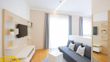 Una sala de estar moderna con un sofá gris, una mesa de centro blanca y un televisor montado en la pared.