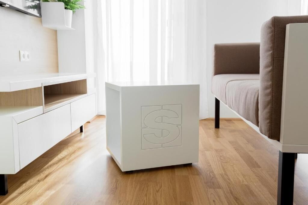 A modern living room with a white cabinet, a side table with a logo, a brown sofa, and a wooden floor.