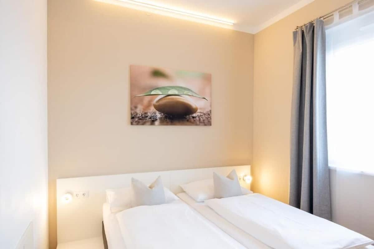 A hotel room with a bed, a wall-mounted picture, and a window with curtains.