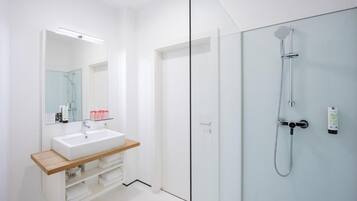 Un baño moderno con cabina de ducha de vidrio, un lavabo blanco con encimera de madera y un espejo sobre el lavabo.