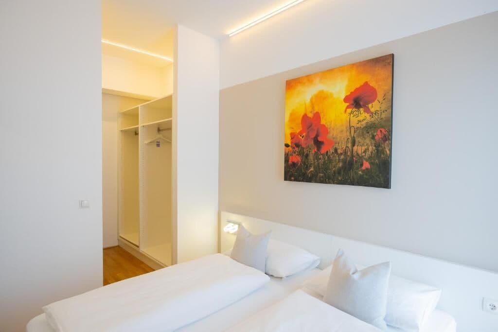 A hotel room with a bed, white bedding, a painting of flowers, and a closet with a mirror.