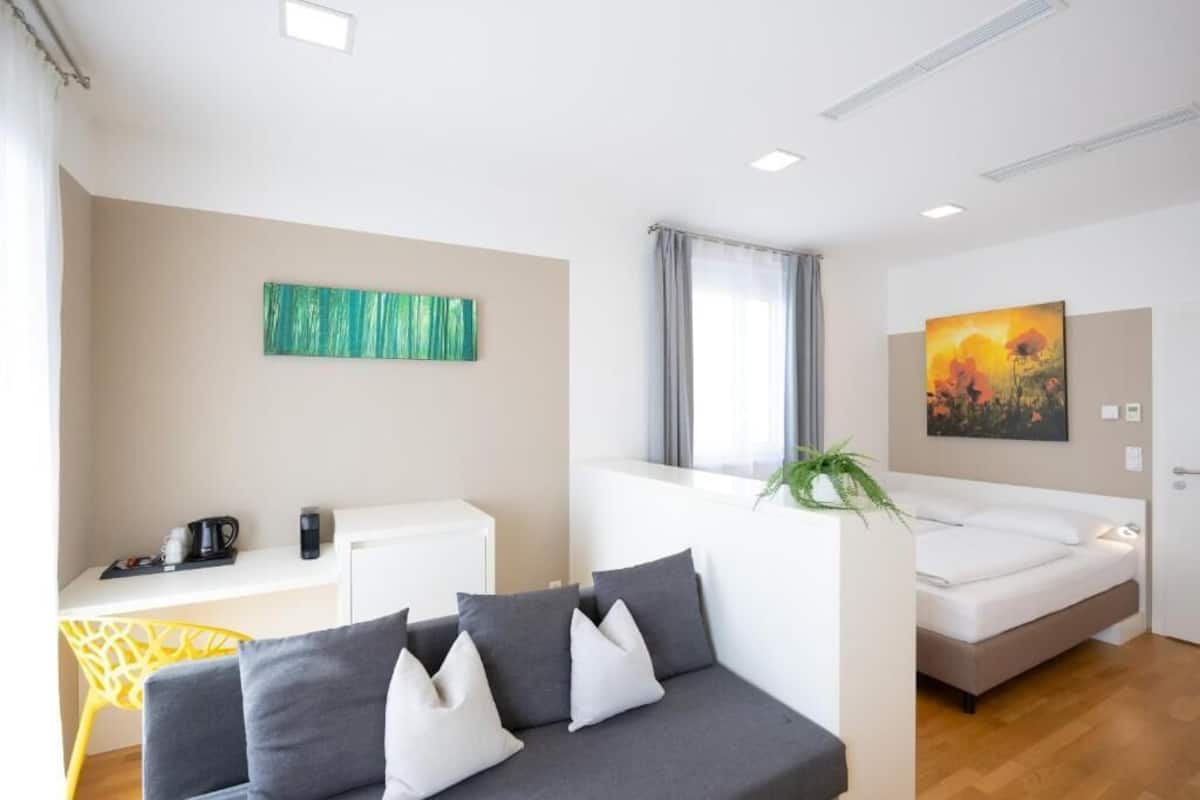 A modern hotel room with a sofa, a bed, a desk, and artwork on the walls.