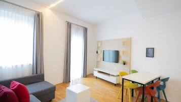 Een moderne woonkamer met een bank, een salontafel, een televisie, een eettafel met kleurrijke stoelen en een witte tv-kast.
