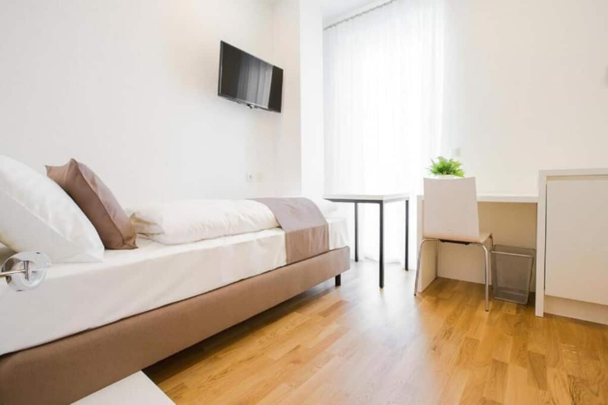 A modern bedroom with a bed, a desk, and a TV.