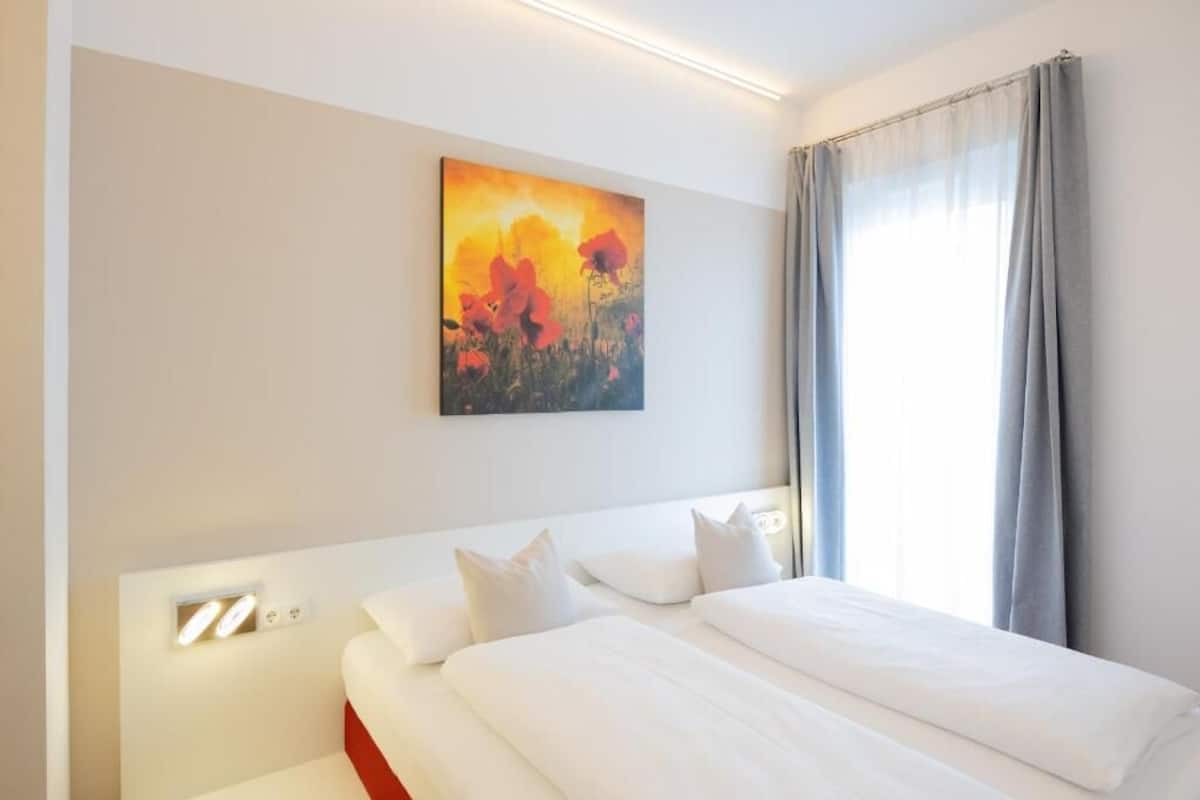 A hotel room with a bed, a painting on the wall, and a window with curtains.