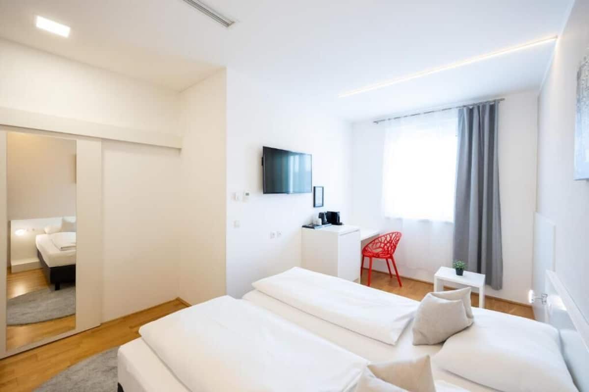 A modern hotel room with a bed, a desk, a TV, and a red chair.