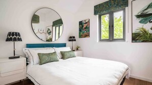 A bedroom with a bed, two bedside tables, a round mirror, and a window with a view of greenery. - Stunning Lodge in Idyllic Setting, Near Cambridge (Bourn)