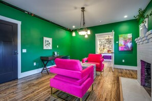 A room with green walls, a wooden floor, a desk, a chair, a sofa, a fireplace, and artwork.